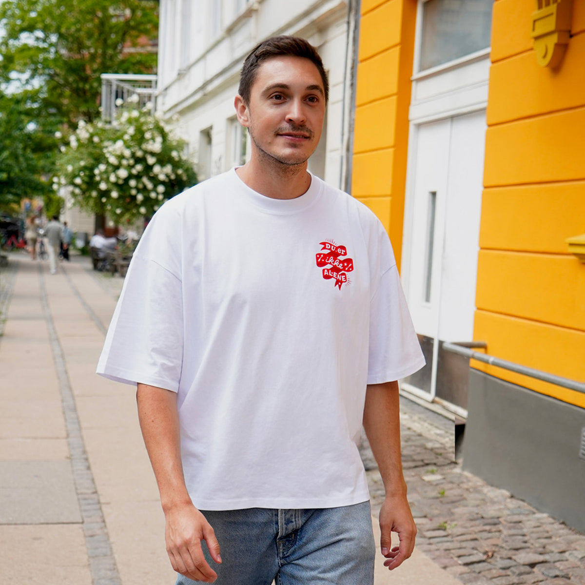 Du er ikke Alene - ung mand iført boxy unisex t-shirt fra Folkekirkens Nødhjælps sommerkollektion.