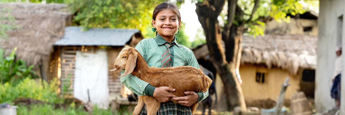 Pige, der holder en ged i armene i en landsby i Nepal. Hun er glad og tilfreds. Giv en ged.